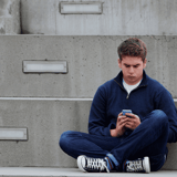 Close-up of teenage boy sitting outdoors on concrete stairs, browsing phone, digital communication, casual urban setting.