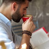 A man drinking coffee while reading a book and using a word counter online tool to check text length.