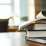 Heart-shaped open book on top of stacked books, representing passion for reading and education. Ideal for literacy or book lover content.