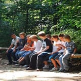 Young kids sitting outdoors on a forest bench during a reading activity.