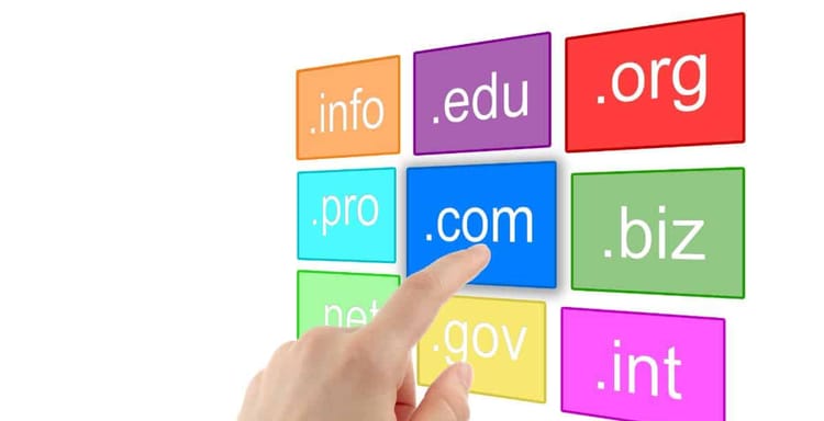 Alt text: Hand pointing at ".com" domain on colorful domain extension blocks.