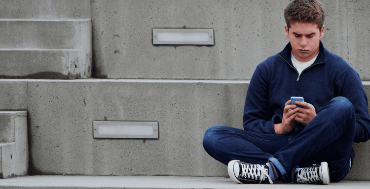 Close-up of teenage boy sitting outdoors on concrete stairs, browsing phone, digital communication, casual urban setting.