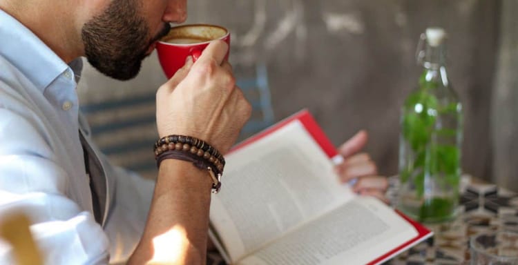 A man drinking coffee while reading a book and using a word counter online tool to check text length.