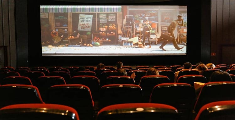 People watching an animated film in a movie theater with red seats.