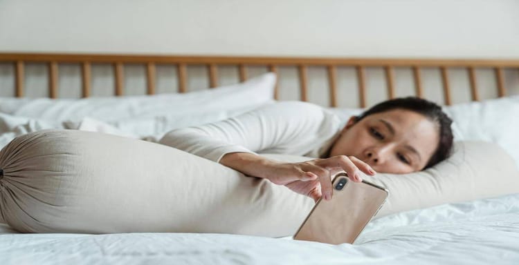 Woman lying in bed using smartphone for word count or writing.