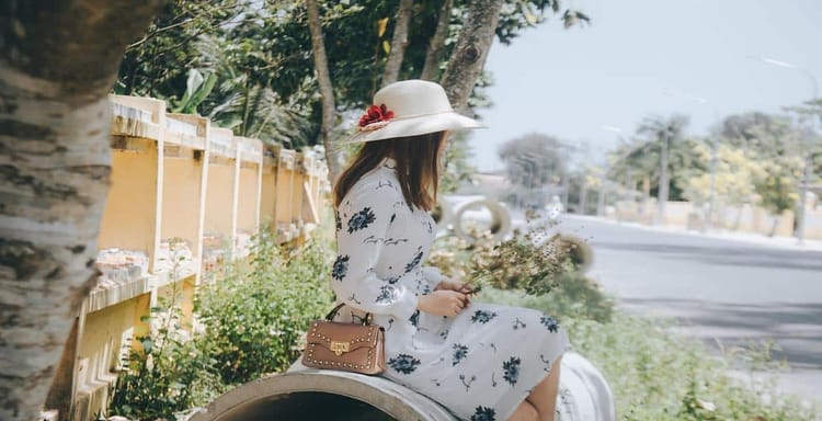 Beautiful woman in floral dress with hat reading outdoors.
