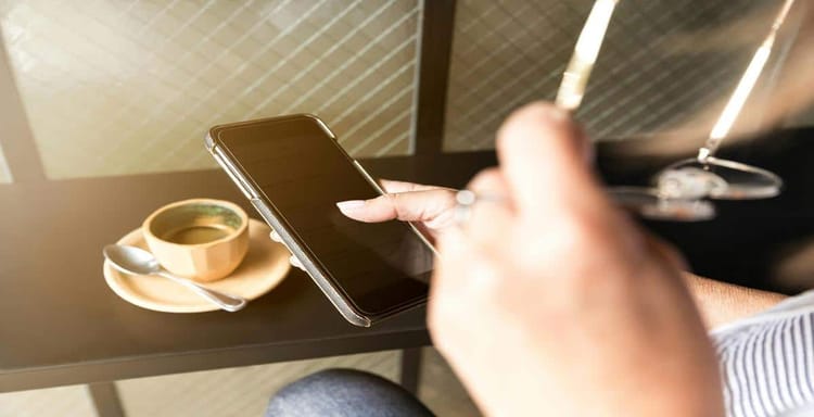 Image shows a smartphone and a coffee cup on a table, focusing on digital writing and productivity.