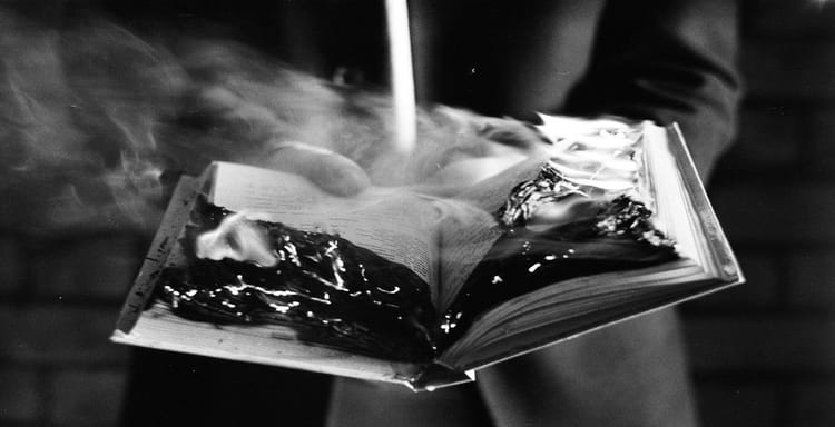 Close-up of a book on fire, emitting smoke, dark tones, and intense flames.