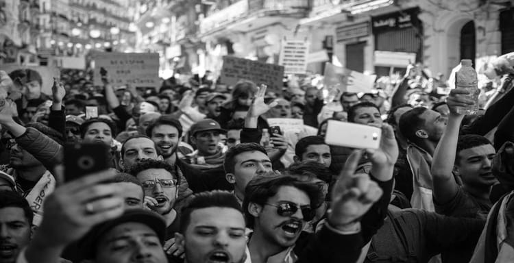 Large crowd of people protesting during a demonstration, holding signs and raising their hands.