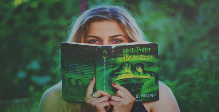 Alt text: Woman reading Harry Potter book outdoors, emphasizing reading and writing tools.
