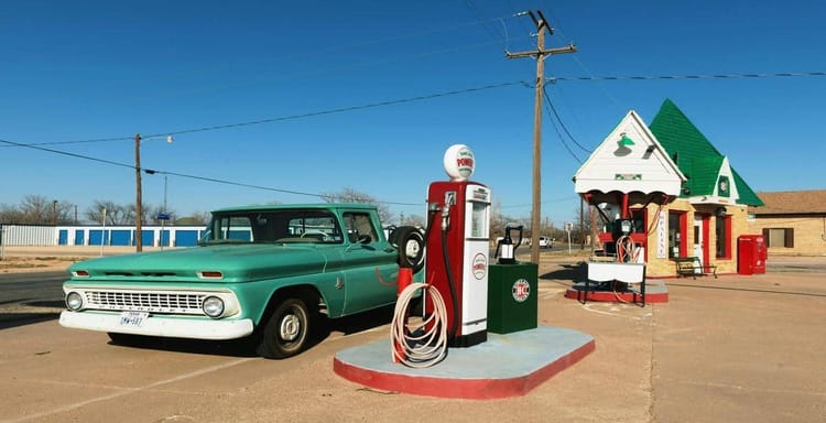 Old-fashioned gas station with vintage car, fueling pumps, and retro roadside architecture.