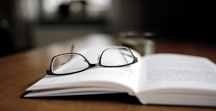 Eyeglasses resting on an open book, emphasizing reading and writing.