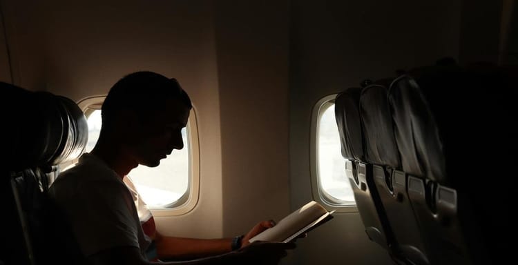 Alt text: Silhouette of a person reading a book on a plane, with airplane windows in the background.