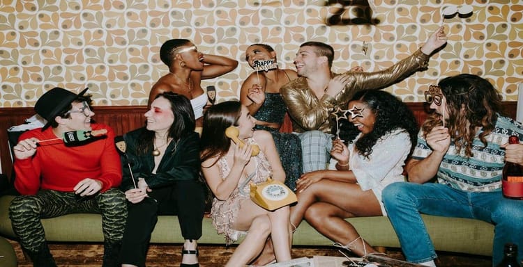 Happy friends having fun at party with props and laughter, celebrating together in a cozy indoor setting.