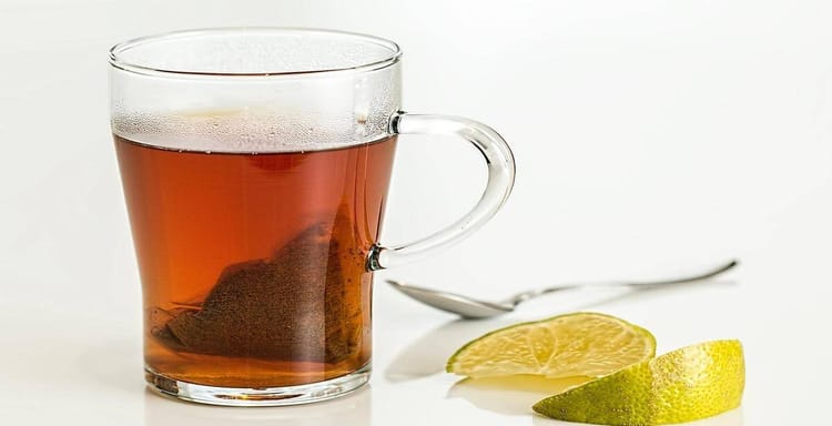 Clear glass cup of hot tea with lemon slice on white background.