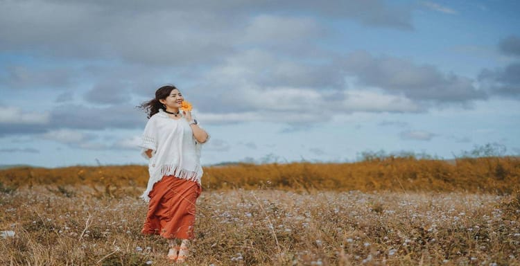 Woman holding flower in scenic field with open sky background.