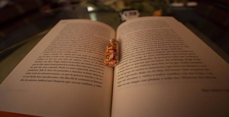 Detailed image showing an open book with a small glass jar filled with dried flower petals placed on the pages.