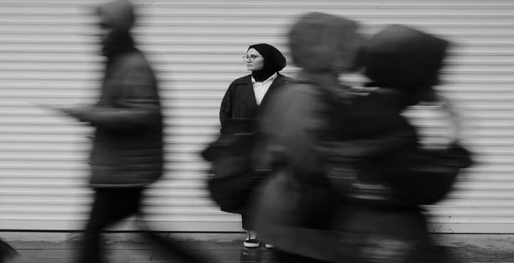 Woman standing still among fast-moving people on city street, monochrome urban scene.