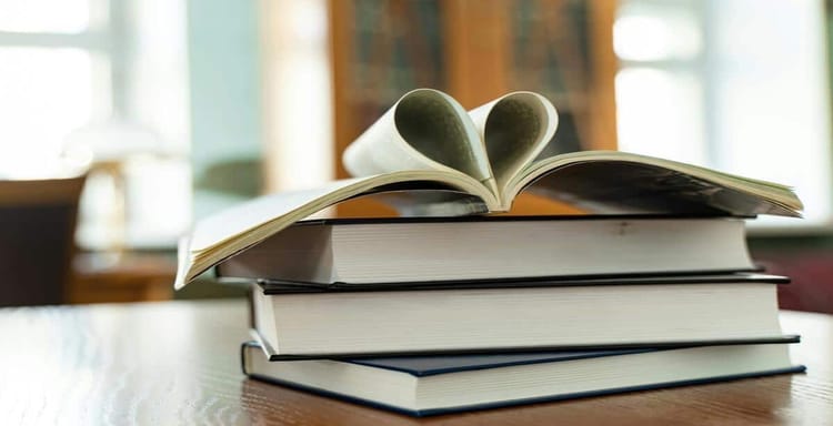 Heart-shaped open book on top of stacked books, representing passion for reading and education. Ideal for literacy or book lover content.