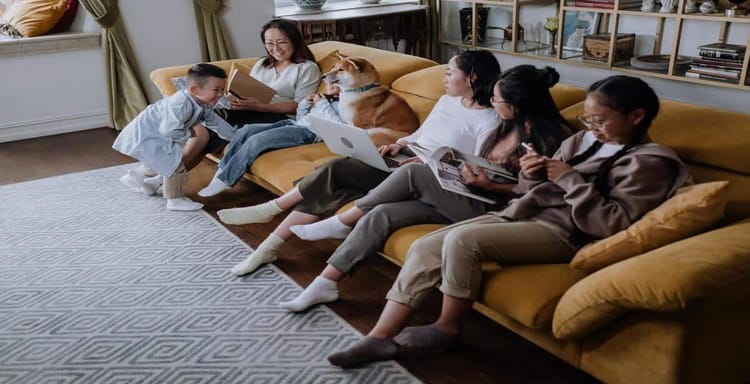 Alt text: Family relaxing on sofa with dog, reading and using devices in cozy living room.