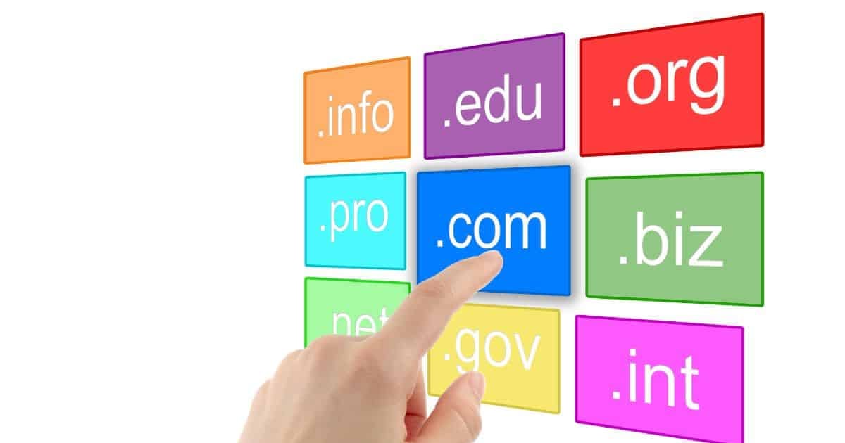 Alt text: Hand pointing at ".com" domain on colorful domain extension blocks.