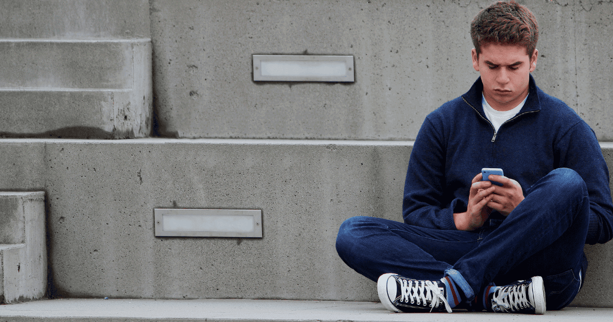 Close-up of teenage boy sitting outdoors on concrete stairs, browsing phone, digital communication, casual urban setting.