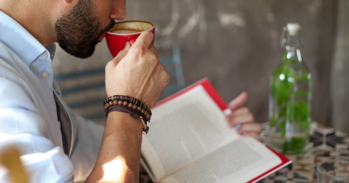 A man drinking coffee while reading a book and using a word counter online tool to check text length.