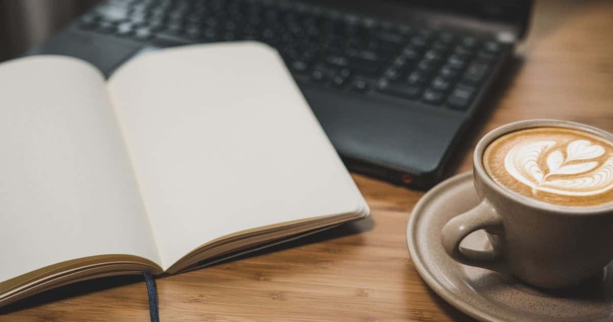Laptop, notebook, coffee for writing and editing text on digital device, workspace, detail, still life, cozy atmosphere, productivity.