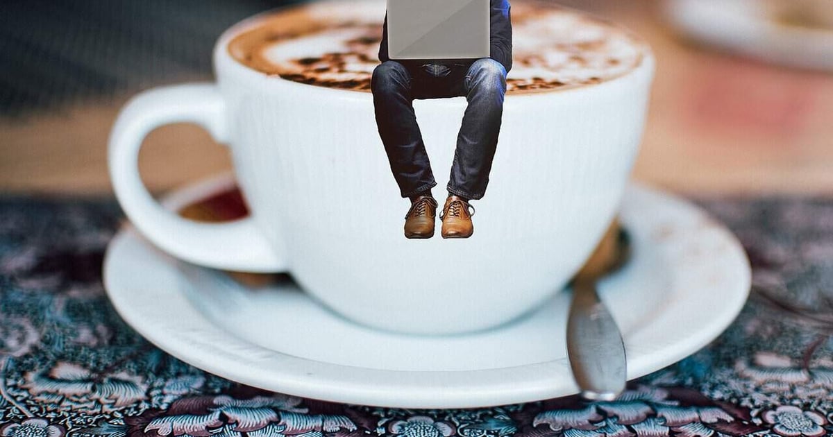 Miniature person with laptop sitting on coffee cup.