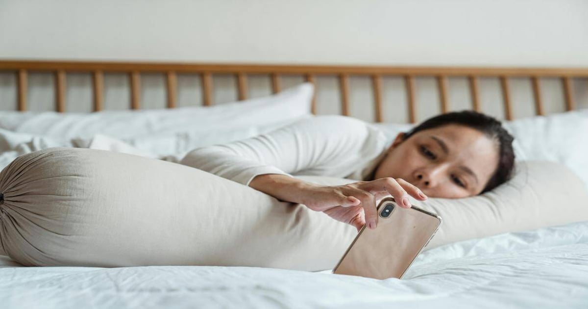 Woman lying in bed using smartphone for word count or writing.