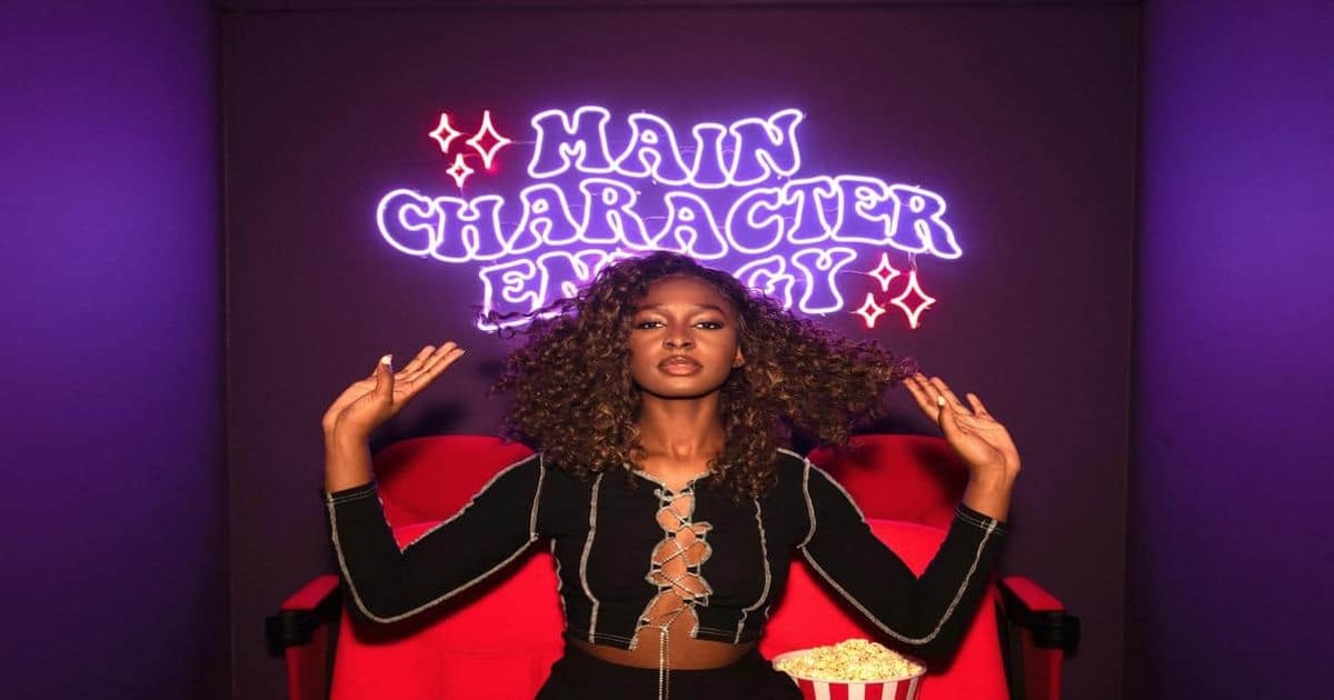 Neon sign reading "Main Character Energy" behind confident woman.