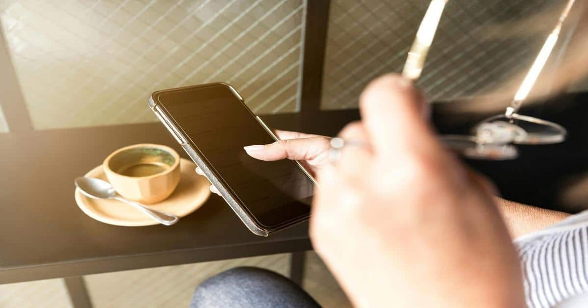 Image shows a smartphone and a coffee cup on a table, focusing on digital writing and productivity.