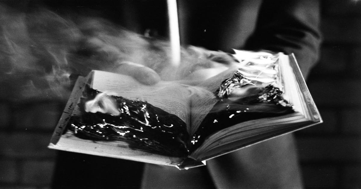 Close-up of a book on fire, emitting smoke, dark tones, and intense flames.