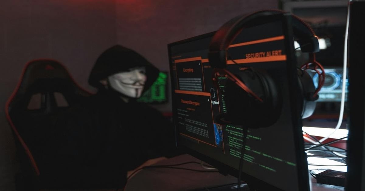 A hacker in a dark hoodie with Guy Fawkes mask working on cybersecurity, surrounded by monitors displaying security alerts and hacking data.