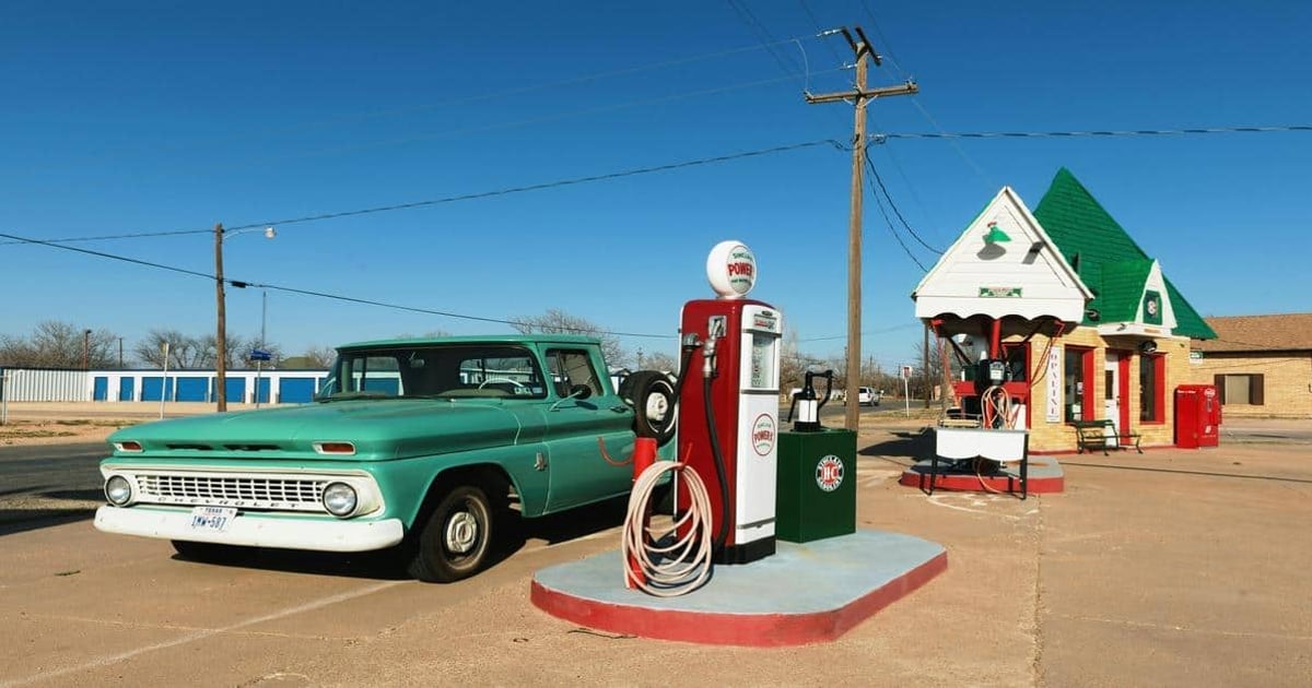 Old-fashioned gas station with vintage car, fueling pumps, and retro roadside architecture.