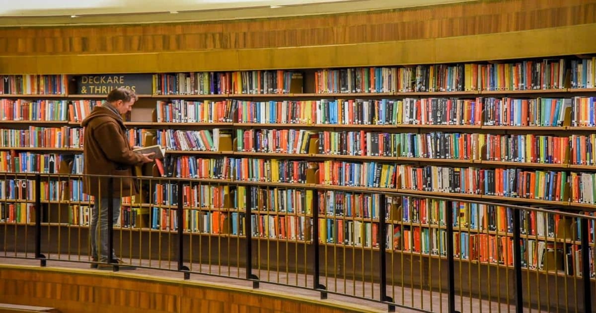 Alt text: Man reading book in a library with colorful shelves of books, emphasizing reading and word counting.