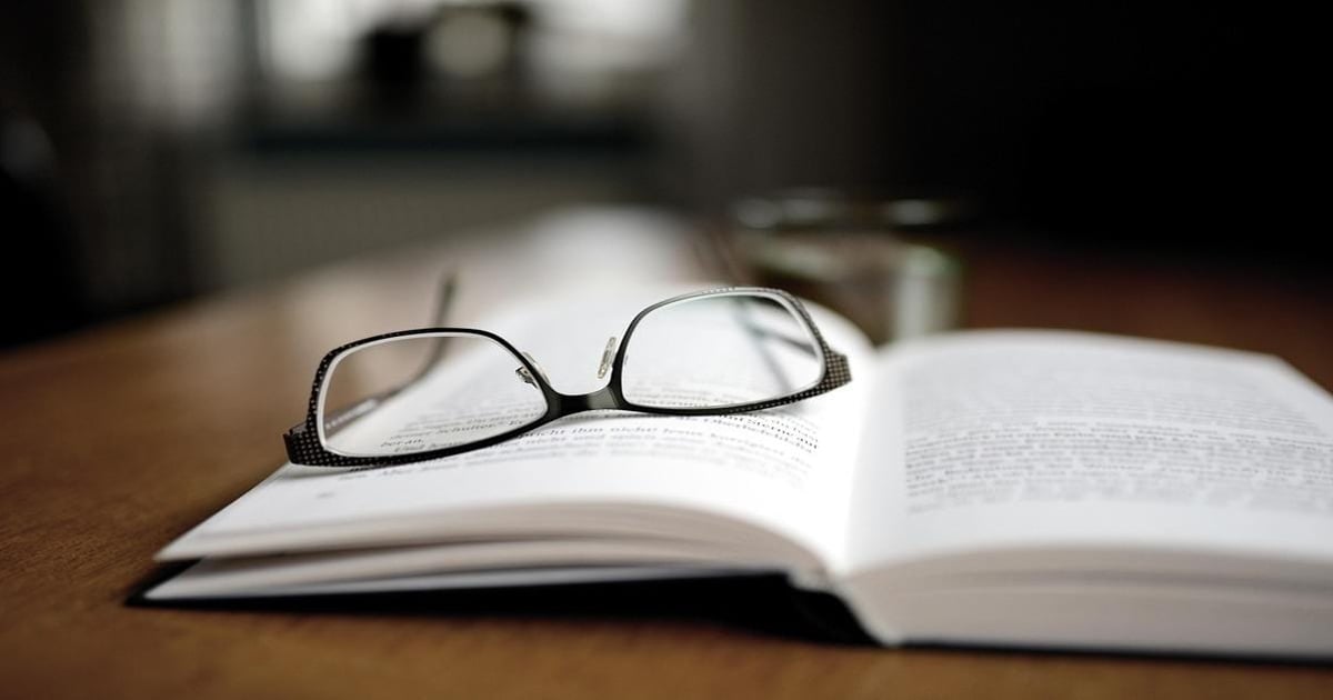 Eyeglasses resting on an open book, emphasizing reading and writing.