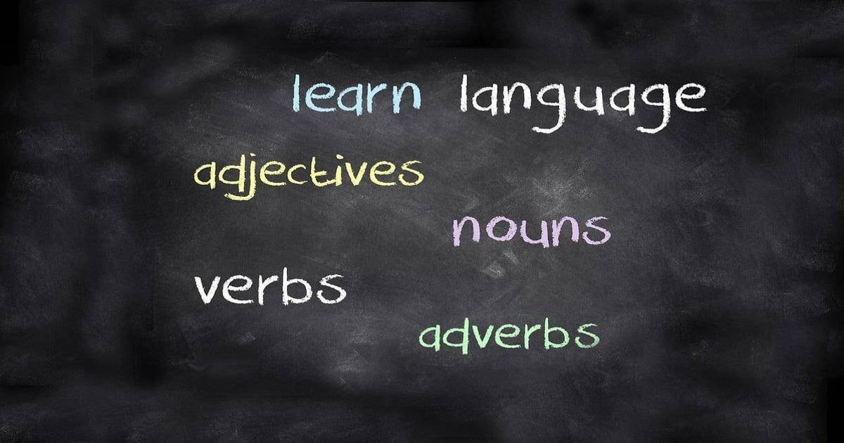 Alt text: Image showing a blackboard with colorful words related to language learning and writing skills like nouns, verbs, adjectives, and adverbs.