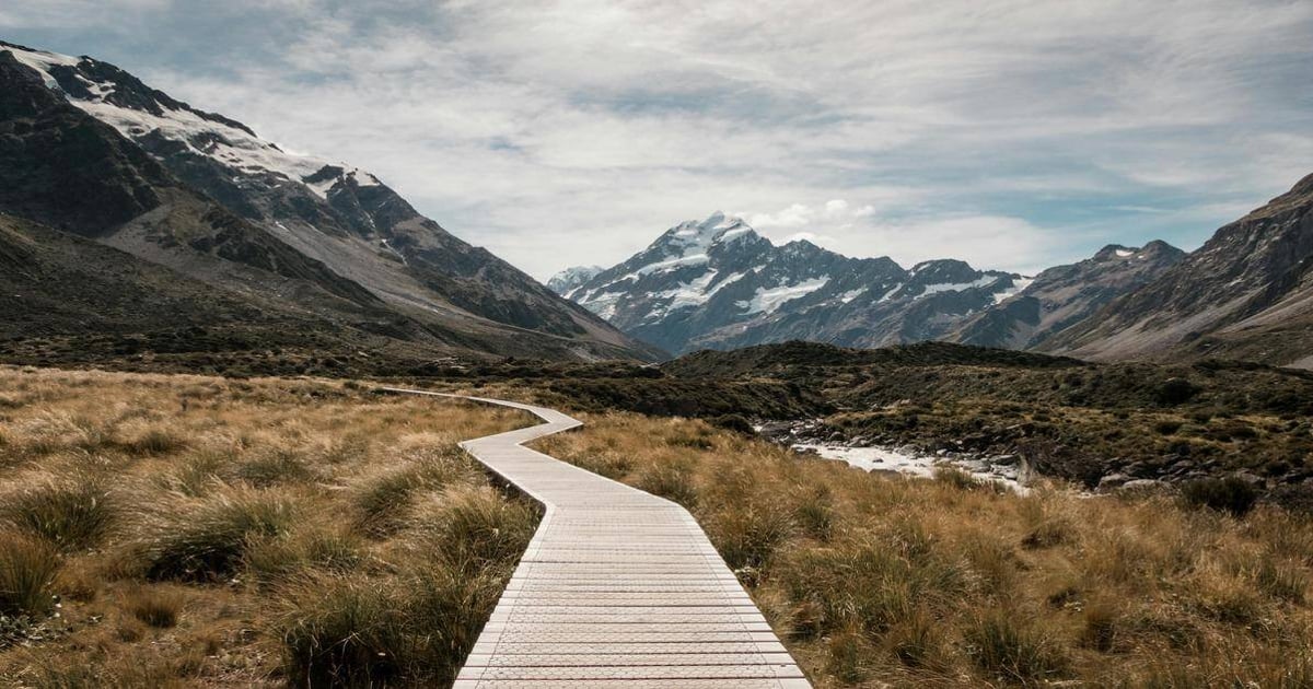 Scenic mountain landscape with wooden walkway and snow-capped peaks in the background.