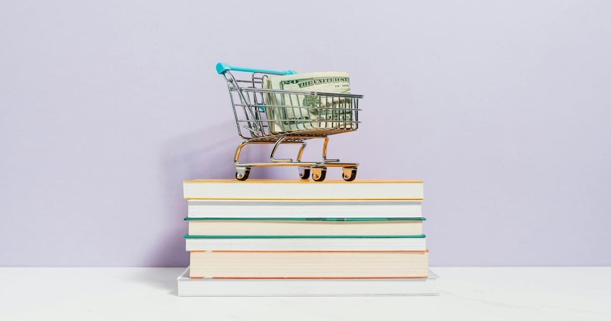 Mini shopping cart with dollar bills on stacked notebooks.
