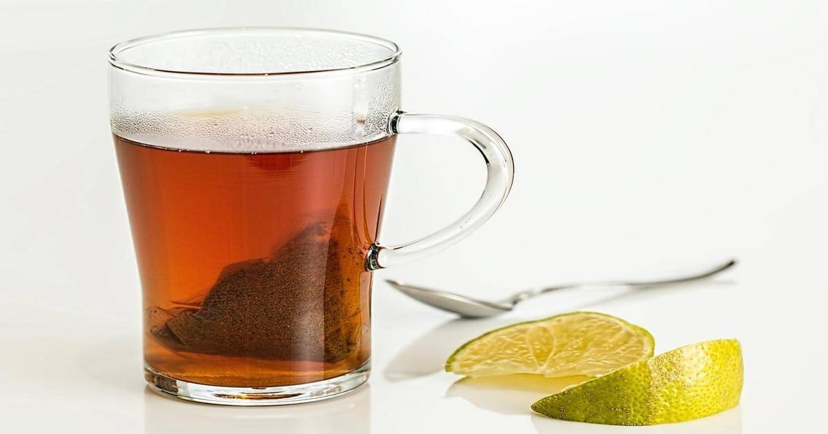 Clear glass cup of hot tea with lemon slice on white background.