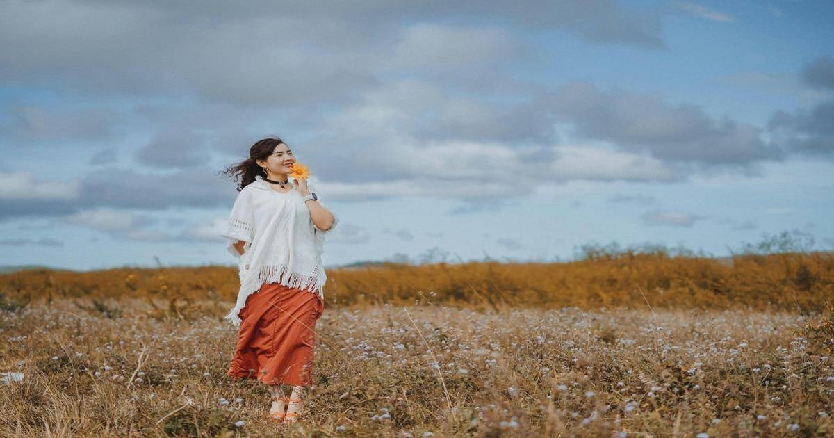 Woman holding flower in scenic field with open sky background.