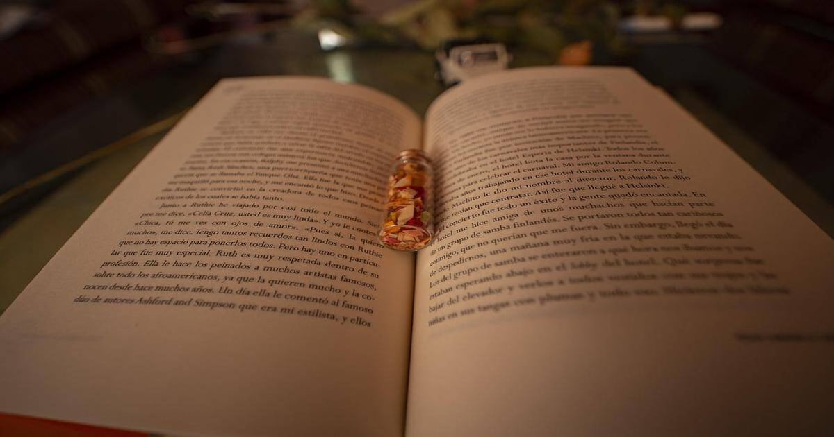 Detailed image showing an open book with a small glass jar filled with dried flower petals placed on the pages.