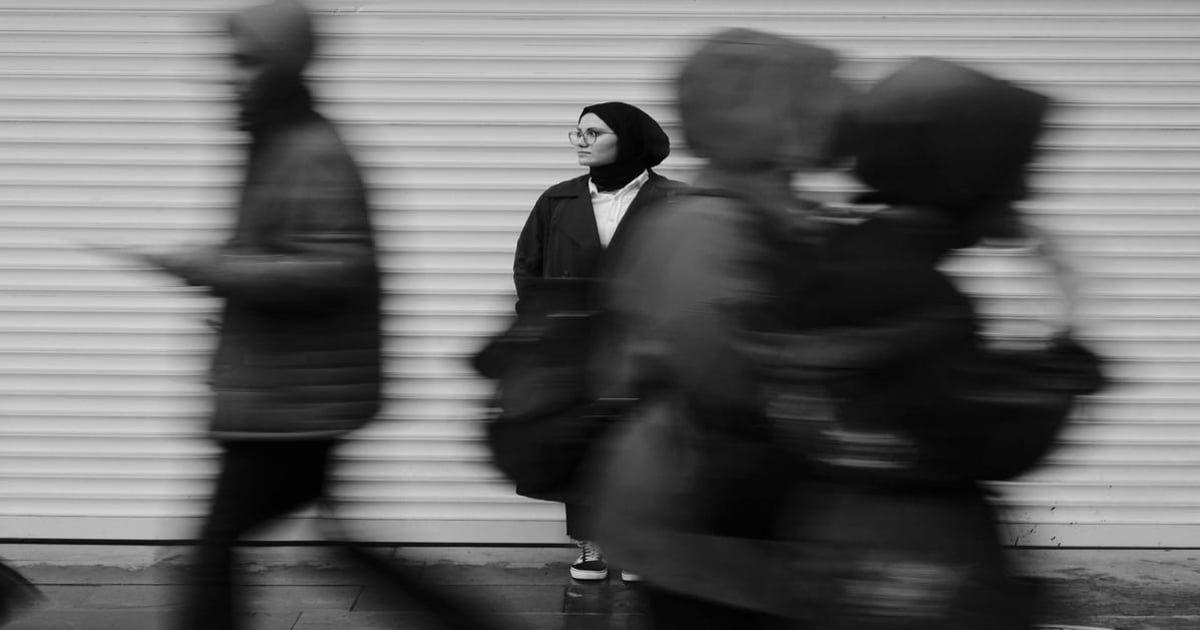 Woman standing still among fast-moving people on city street, monochrome urban scene.