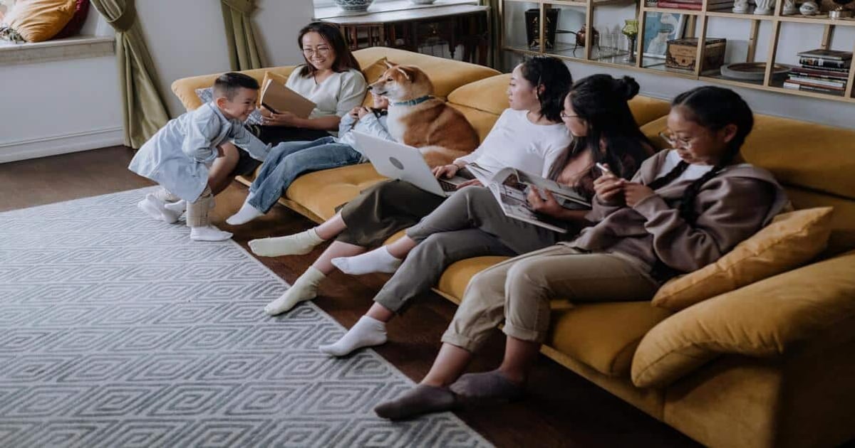 Alt text: Family relaxing on sofa with dog, reading and using devices in cozy living room.
