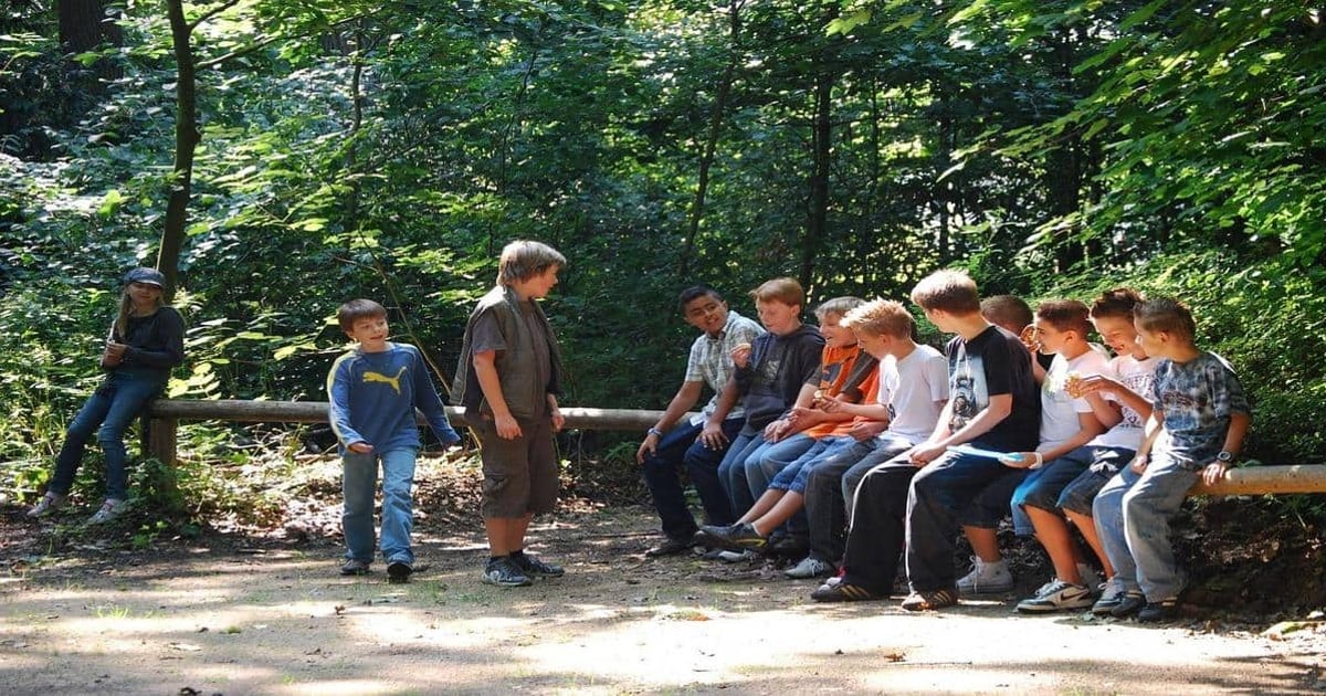 Young kids sitting outdoors on a forest bench during a reading activity.